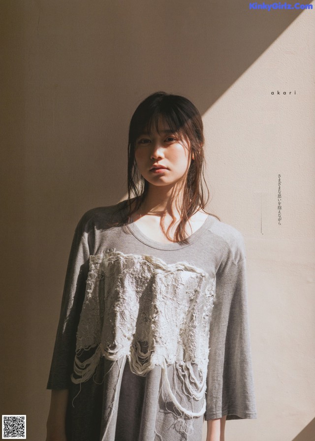 A woman standing in front of a wall wearing a gray shirt.