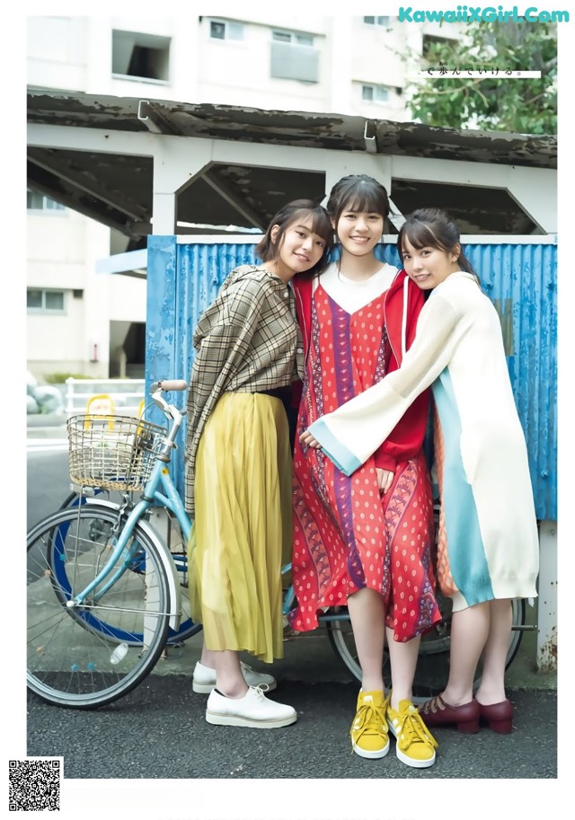 A group of three women standing next to each other near a bike.