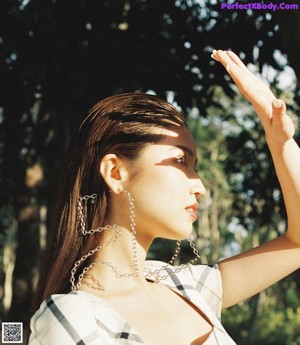 A woman leaning against a tree in a plaid dress.