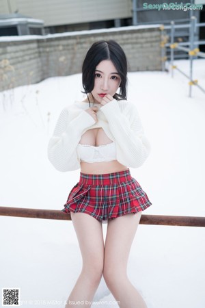 A woman in a white sweater and red plaid skirt posing in the snow.