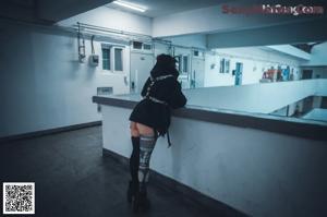 A woman in a black jacket and black stockings holding a gun.