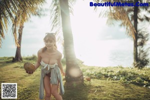 A woman in a bikini standing next to a palm tree.