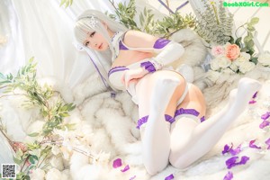 A woman in a white and purple outfit sitting on a bed.