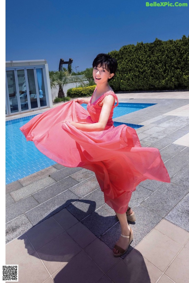 A woman in a pink dress standing by a swimming pool.