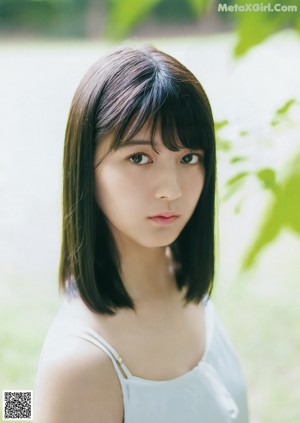 A woman in a black tank top leaning against a wall.