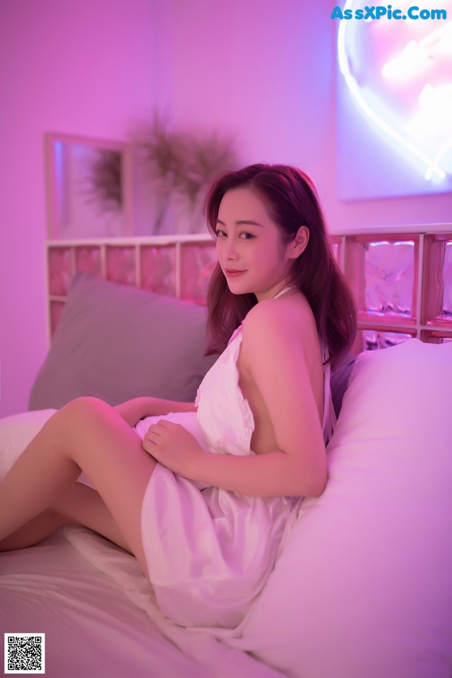 A woman sitting on a bed in a white dress.