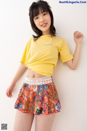 A young woman in a yellow shirt and colorful skirt.