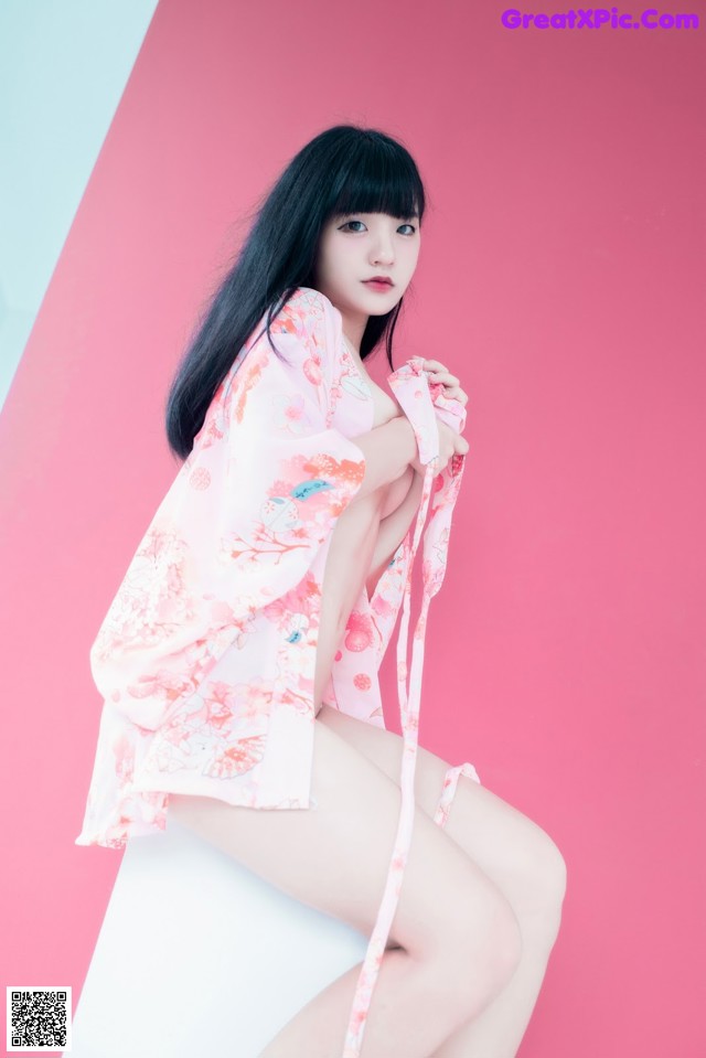 A woman in a pink kimono sitting on a white chair.