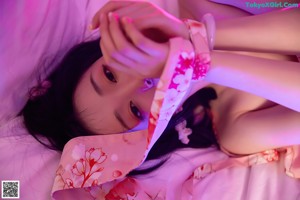 A woman in a pink kimono sitting on a bed.