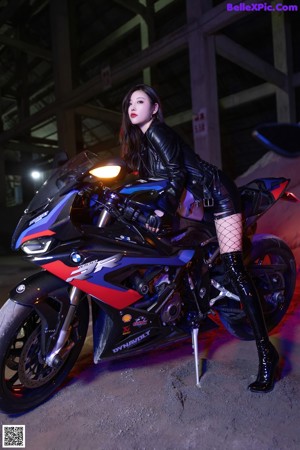 A woman in a black bodysuit and fishnet stockings standing next to a motorcycle.
