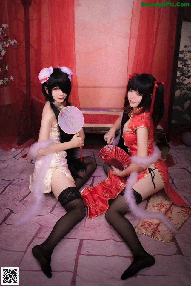 Two women dressed in chinese clothing sitting on a bed.