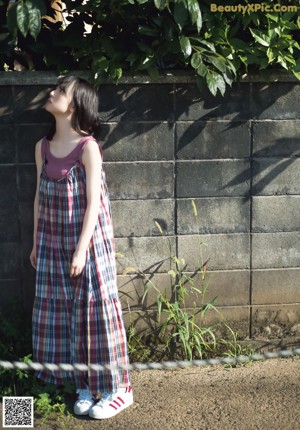 A woman in a plaid dress leaning against a wall.