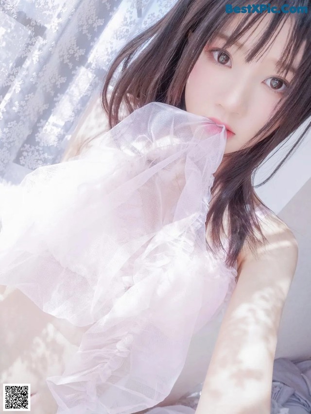 A woman in a white dress sitting on a bed.