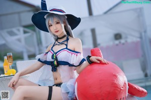 A woman in a sailor outfit sitting on a lounge chair by a pool.