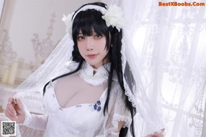 A woman in a white lingerie sitting on a bed holding a gun.