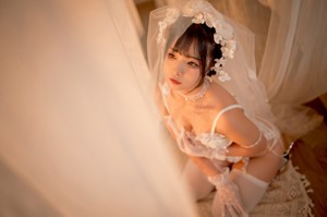 A woman in a white lingerie sitting on a bed.