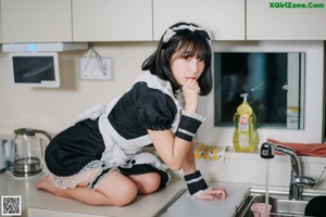 A woman in a maid outfit standing in a kitchen.