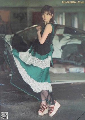 A woman in a green and white dress standing in front of a car.