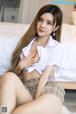 A woman in a plaid skirt is posing on a bed.