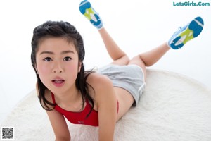 A young girl laying on a white rug with her hands on her stomach.