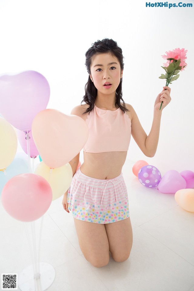 A woman in a pink top and shorts holding a bunch of balloons.