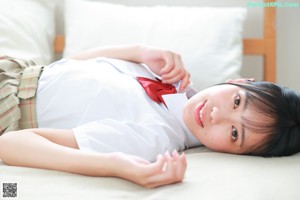 A woman in a school uniform sitting on a bed.