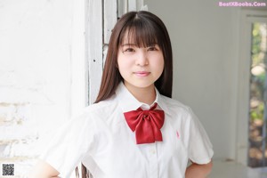 A young woman in a school uniform sitting on a stool.