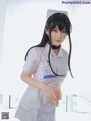 A woman in a white shirt and black stockings sitting on a bed.