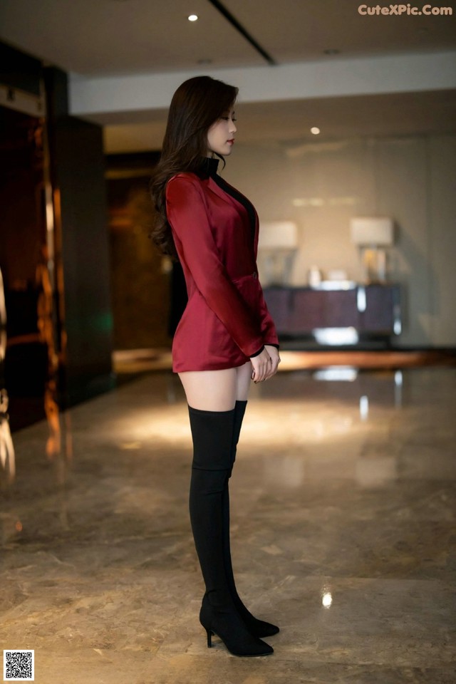 A woman in a red blazer and black thigh high boots.